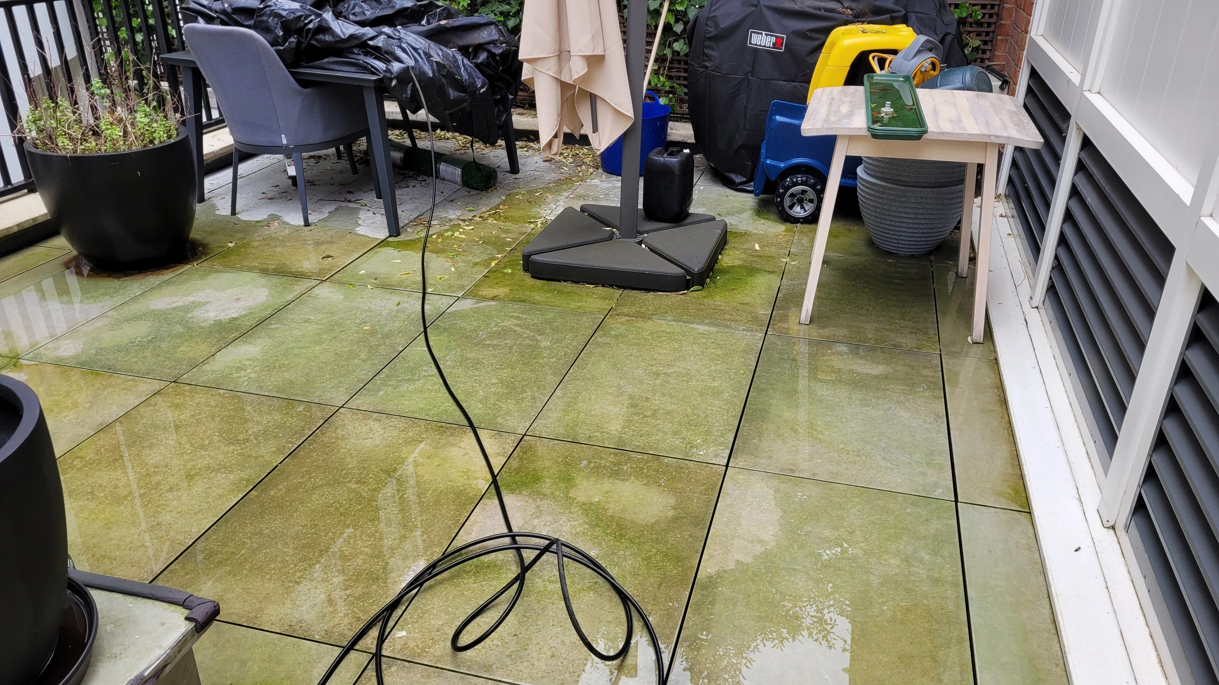 Dirty outdoor porcelain patio covered in green algae and black spot lichen before cleaning in Crawley